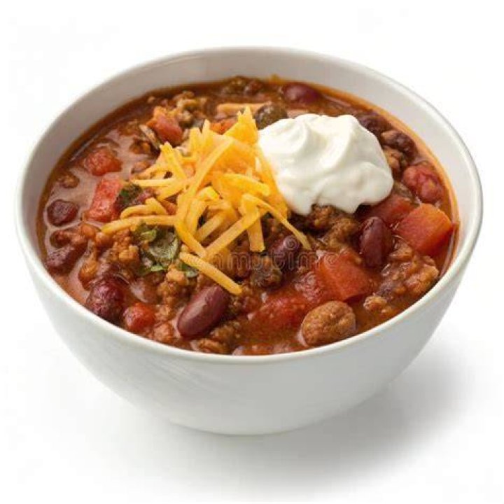 Chili in a white bowl with cheese in the background.