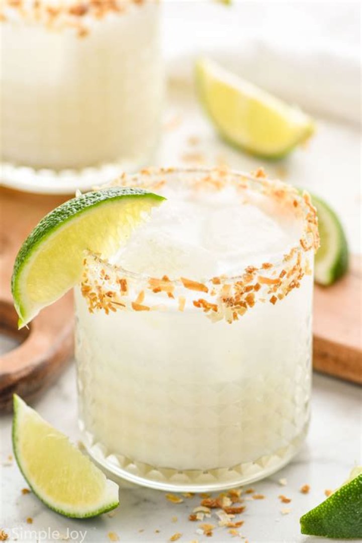 Closeup of a coconut margarita in a glass garnished with toasted coconut and lime
