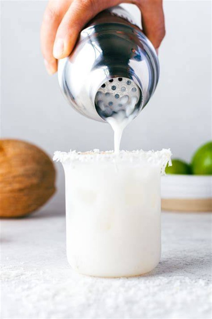 Coconut margarita being poured from a cocktail shaker into a glass