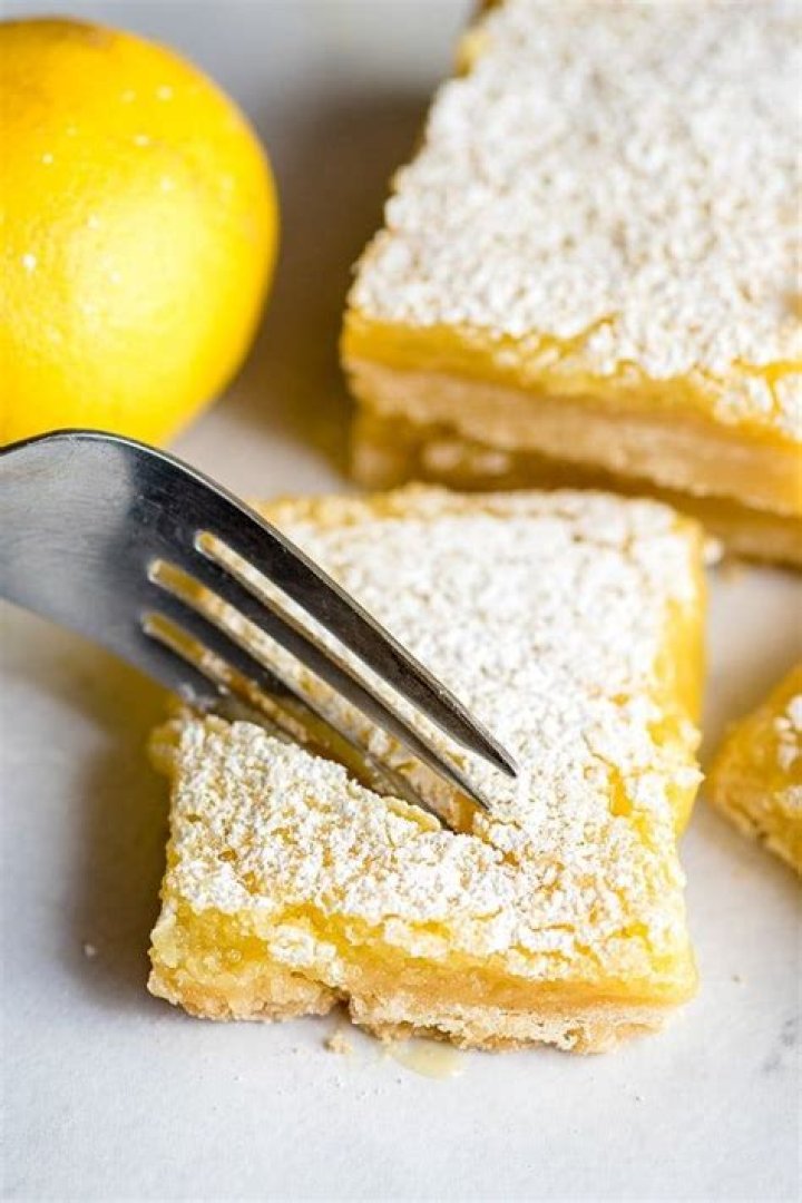 Lemon bar topped with pink frosting and garnished with a lemon slice and raspberry.
