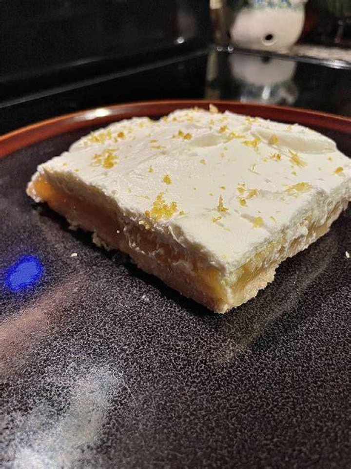 Lemon Bar topped with whipped cream on a spatula.
