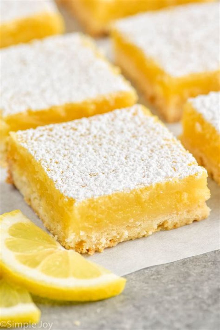 Lemon bars on a baking rack with lemon wedges.