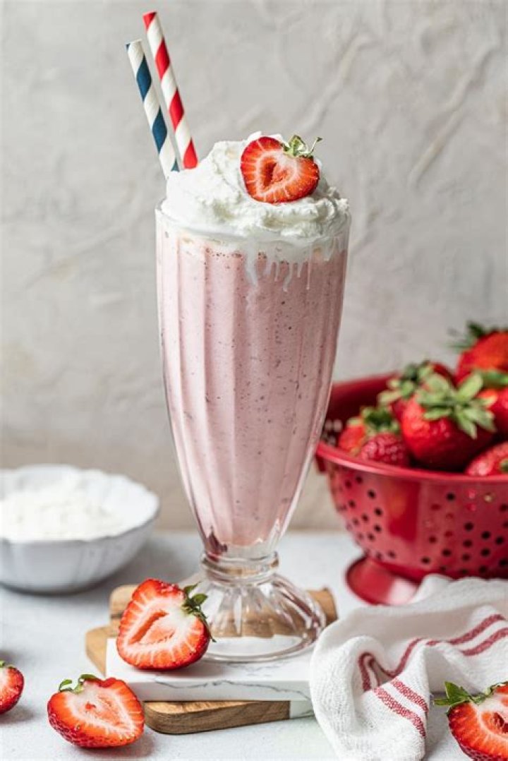 Strawberry milkshake in a glass topped with whipped cream and strawberries.