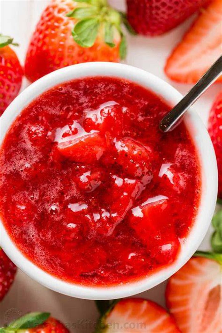 Strawberry sauce on top of yogurt in a white bowl on a blue plate.
